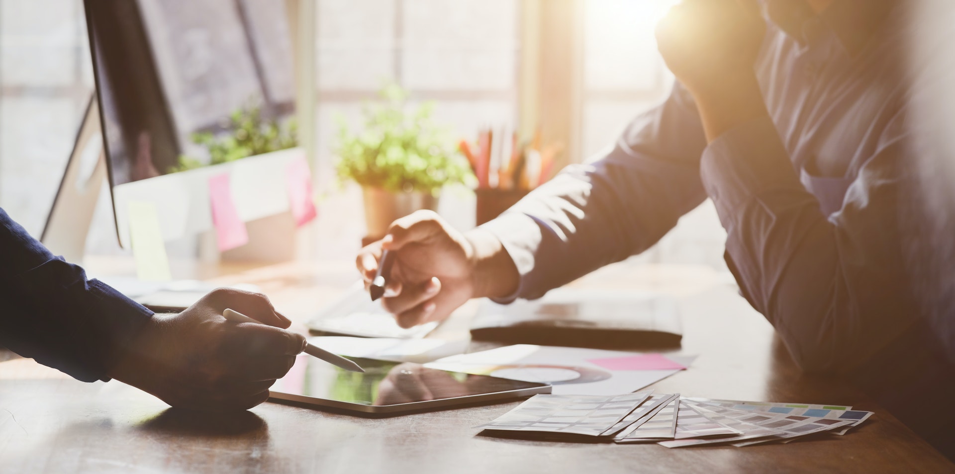 two hands in the foreground on an office setting background with a plant, and tablet